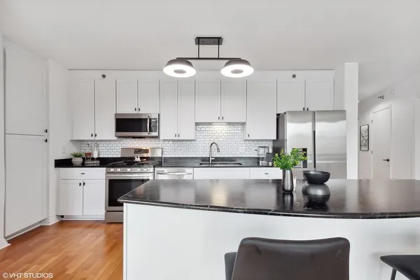 a kitchen with stainless steel appliances granite countertop a sink a stove top oven a refrigerator with white cabinets and wooden floor