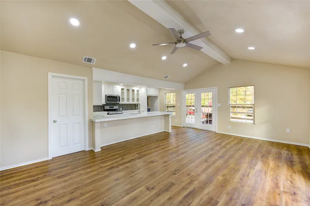 a view of an empty room and kitchen with wooden floor