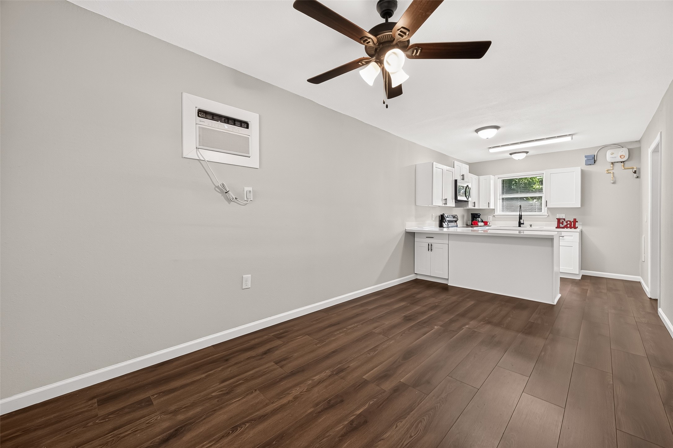 103 East Janisch Road Houston, TX 77022 - Photo 18 of 27 Modern open-concept kitchen and living area featuring sleek white cabinetry, a ceiling fan, and rich laminate-wood flooring for a warm, inviting atmosphere.