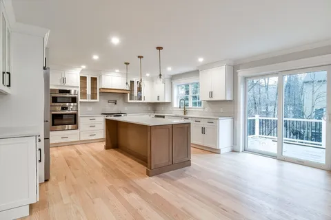 a kitchen with stainless steel appliances kitchen island granite countertop a stove a sink and white cabinets with wooden floor