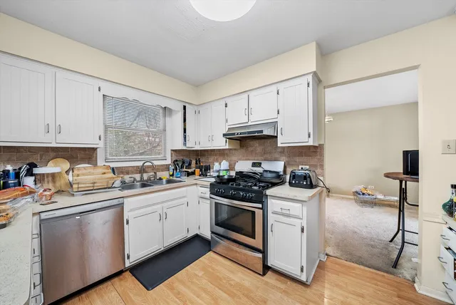 a kitchen with stainless steel appliances granite countertop a stove a sink dishwasher and white cabinets with wooden floor