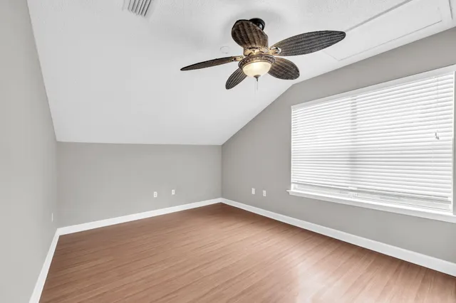 an empty room with wooden floor ceiling fan and windows
