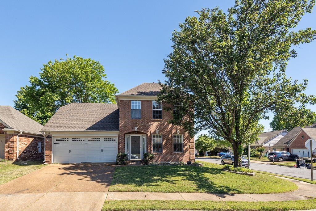 9768 Riggin Drive Memphis, TN 38002 - Photo 2 of 32 Brick facade two-story residence featuring an attached two-car garage, pitched shingle roof, and a mature shade tree