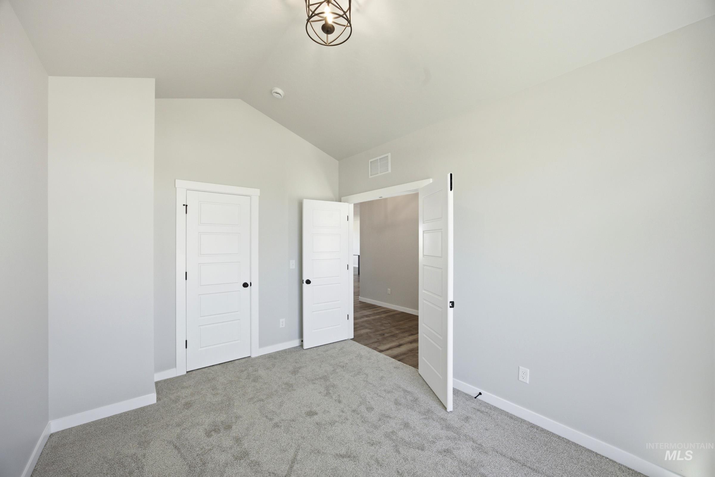 4344 East Rincon Drive Meridian, ID 83642 - Photo 10 of 26 Neutral wall paint, textured carpet flooring, vaulted ceiling, white paneled doors with black hardware, and an overhead light fixture