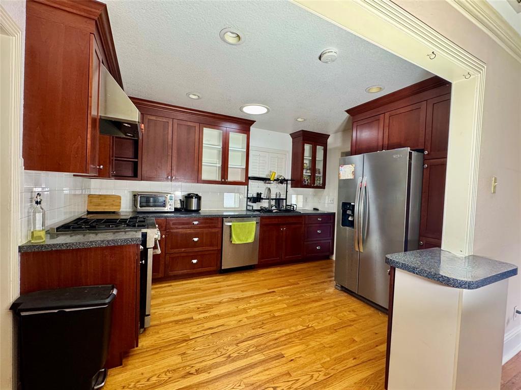 6712 Timothy Drive Dallas, TX 75227 - Photo 5 of 20 Kitchen featuring stainless steel appliances, glass fronted cabinets, light wood-style flooring, exhaust hood, and bold wood finish cabinets