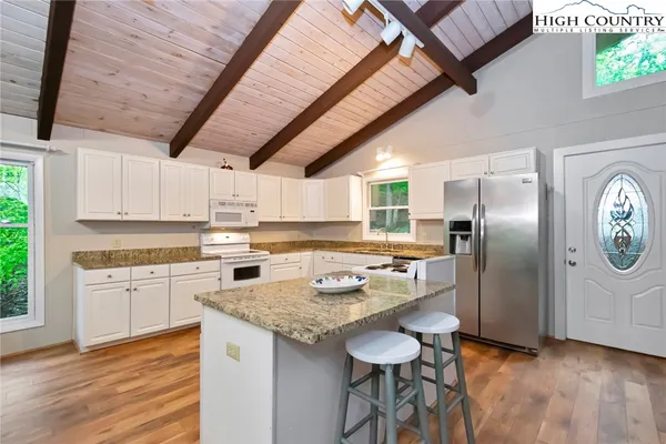 a kitchen with granite countertop a refrigerator a stove a sink dishwasher and white cabinets with wooden floor