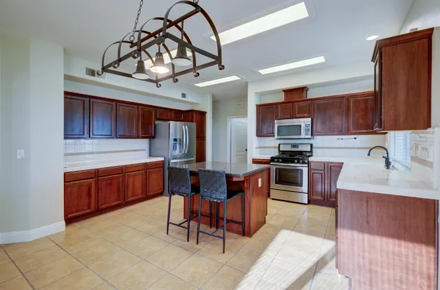 a kitchen with stainless steel appliances granite countertop a sink dishwasher a stove a refrigerator cabinets and a dining table with wooden floor