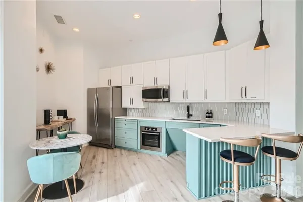 a kitchen with kitchen island granite countertop a sink a stove a refrigerator and white cabinets with wooden floor