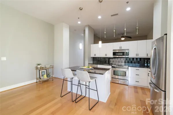 a kitchen with stainless steel appliances kitchen island granite countertop a stove top oven a sink dishwasher and a refrigerator with wooden floor