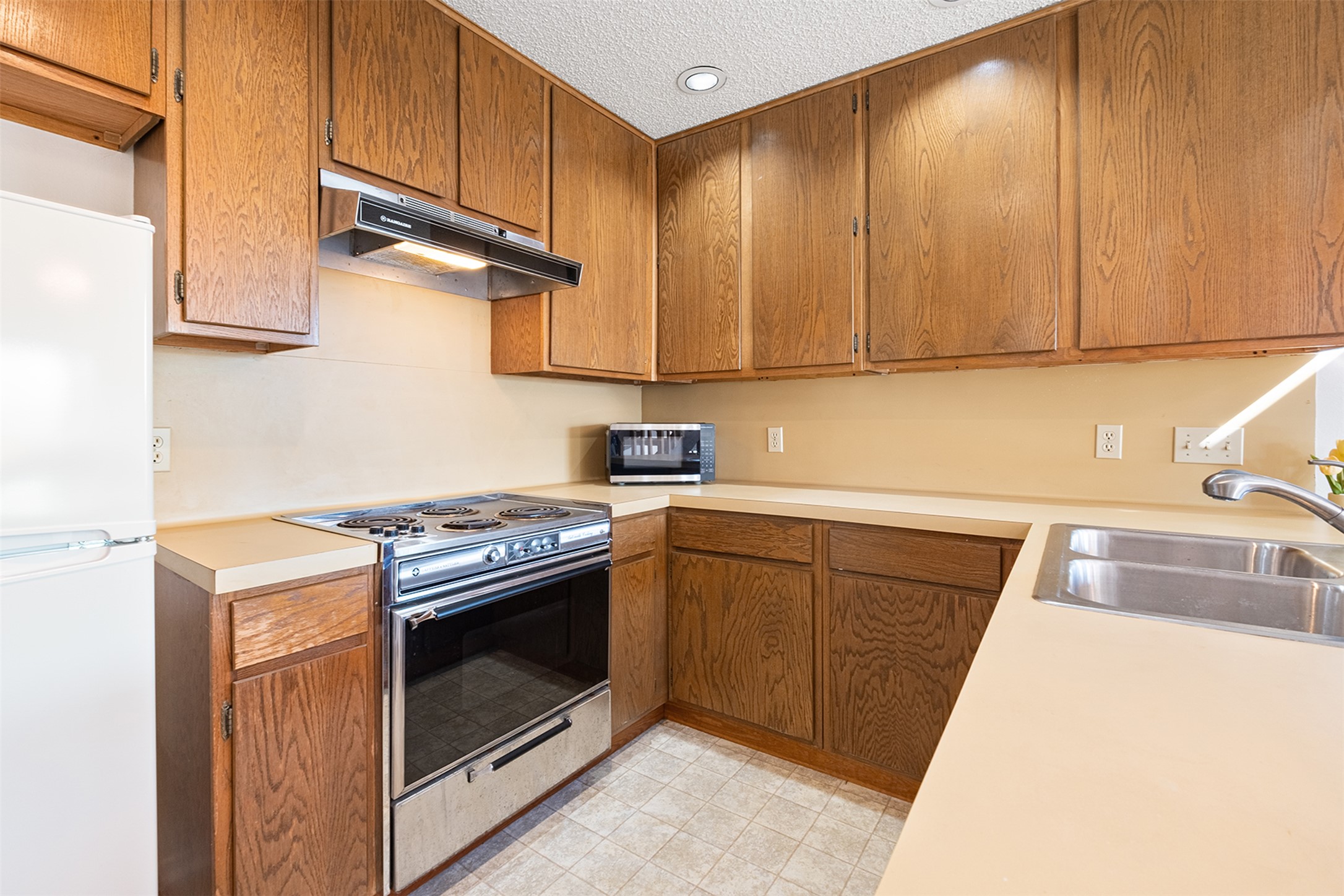 1748 Ohlen Road, Unit 16 Austin, TX 78757 - Photo 14 of 38 Kitchen featuring stainless steel appliances, light countertops, wood finish cabinetry, a textured ceiling, and light floors