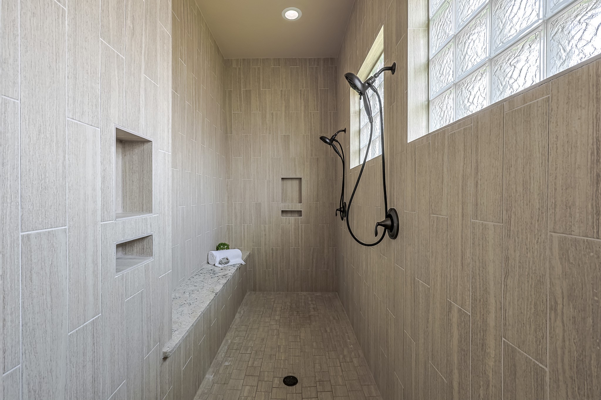 515 Mill Creek Road Pinehurst, TX 77362 - Photo 29 of 48 This spacious walk-in shower has elegant beige tiles, dual shower heads, glass block windows for natural light, built-in shelves, and a bench for convenience.