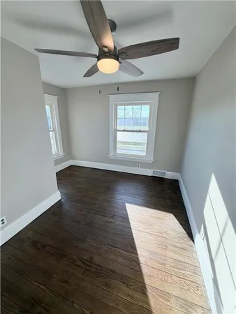 an empty room with wooden floor chandelier fan and windows