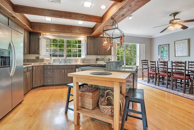 a kitchen with stainless steel appliances granite countertop a stove a refrigerator a sink a dining table and chairs with wooden floor