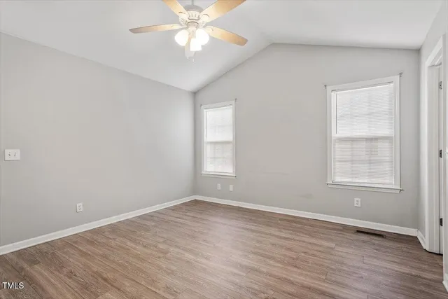 an empty room with wooden floor fan and windows
