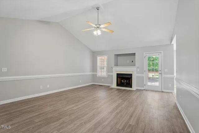 an empty room with wooden floor fireplace cabinet and windows