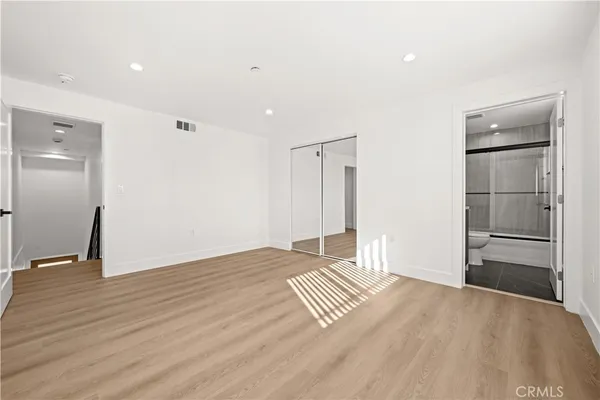 a view of empty room with wooden floor and kitchen