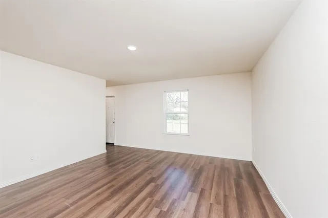 a view of an empty room with wooden floor and window