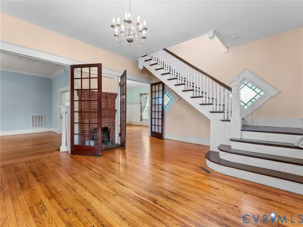 a view of an empty room with wooden floor and a chandelier