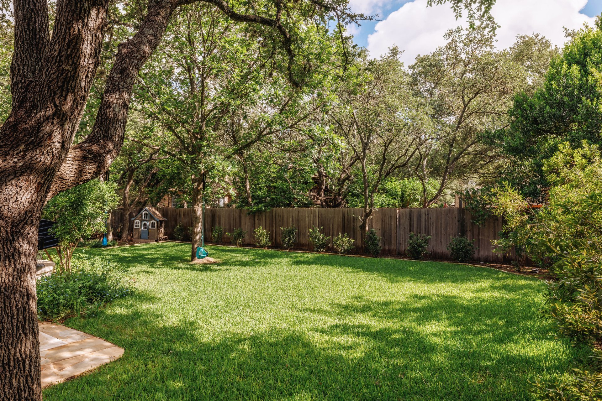 5512 Ballenton Lane Austin, TX 78739 - Photo 40 of 40 A verdant lawn invites outdoor enjoyment, bordered by a wooden privacy fence and mature trees providing natural shade.