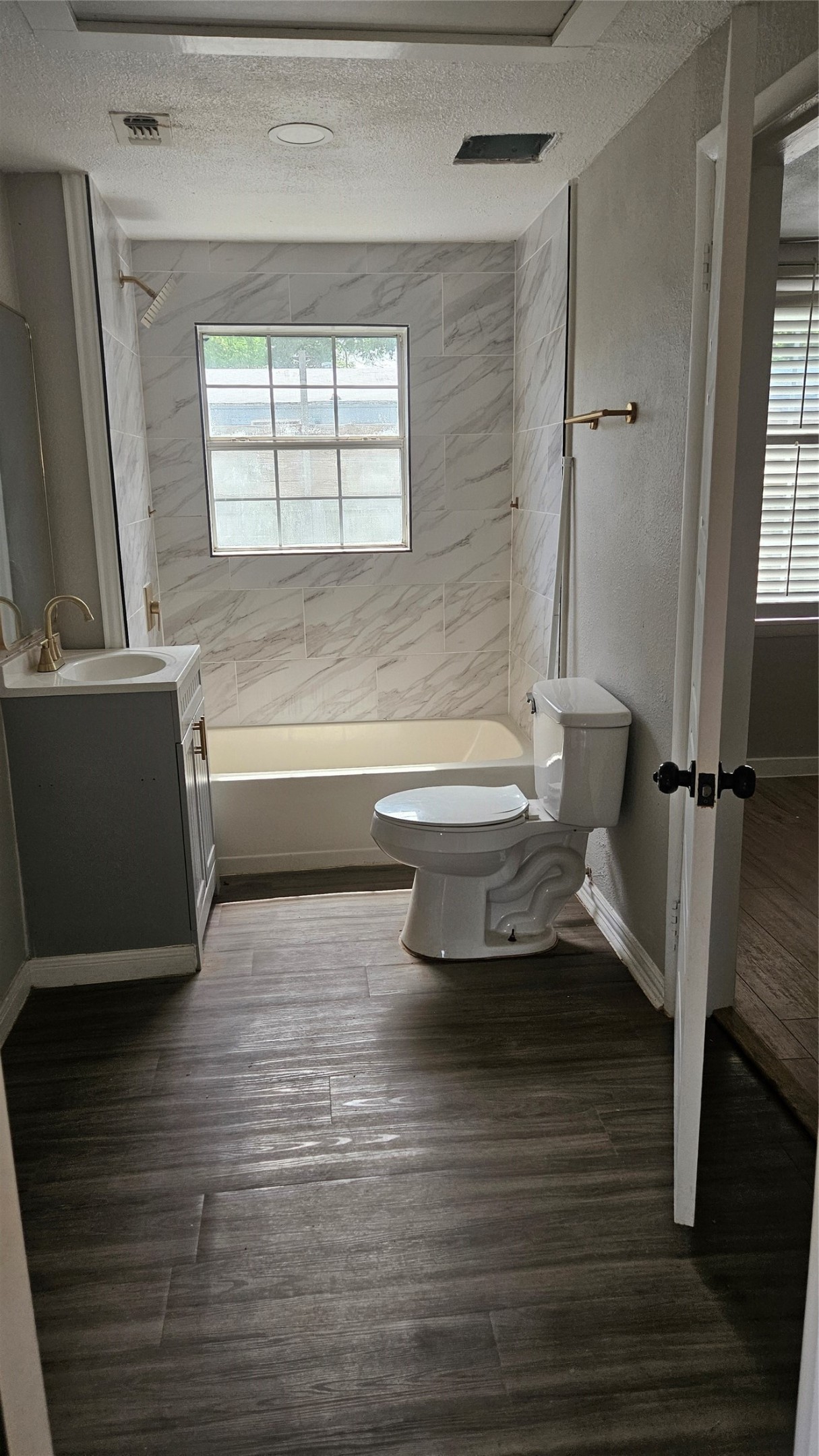 2415 Perry Street Baytown, TX 77521 - Photo 12 of 23 This second bathroom features a modern design with wood-style flooring and marble-patterned wall tiles. It is equipped with a bathtub, toilet, and vanity sink. A window allows natural light to brighten the space. This second bath is located between the 2nd and 3rd bedrooms.