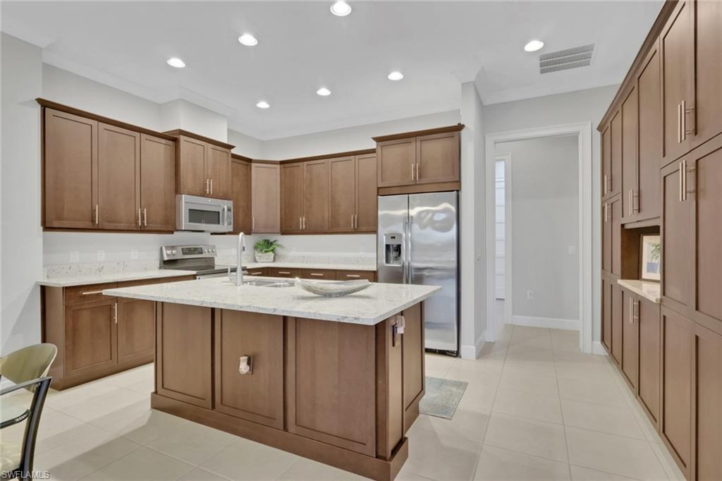 6809 Bequia Way Naples, FL 34113 - Photo 11 of 46 Kitchen with stainless steel appliances, light stone countertops, a center island with sink, brown cabinets, and recessed lighting