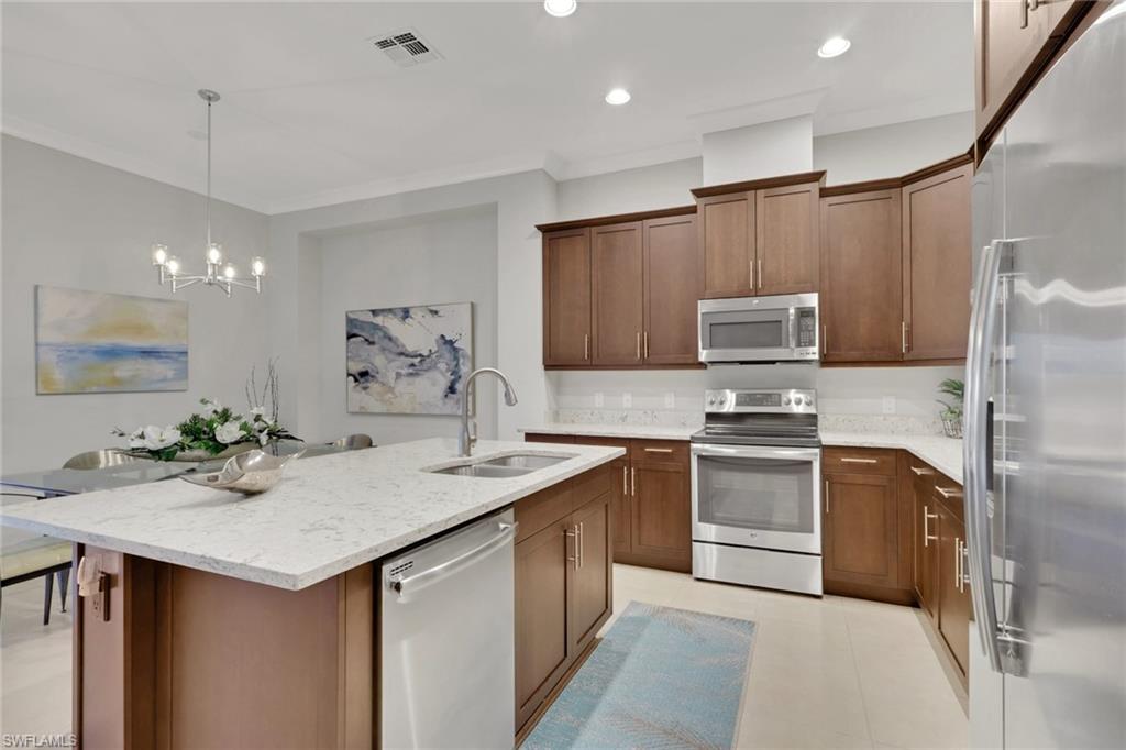 6809 Bequia Way Naples, FL 34113 - Photo 13 of 46 Kitchen with stainless steel appliances, light stone countertops, an island with sink, decorative light fixtures, and crown molding