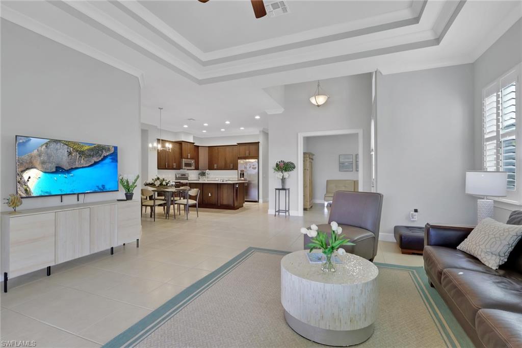 6809 Bequia Way Naples, FL 34113 - Photo 5 of 46 Living area featuring ceiling fan, light tile patterned flooring, a chandelier, ornamental molding, and a tray ceiling