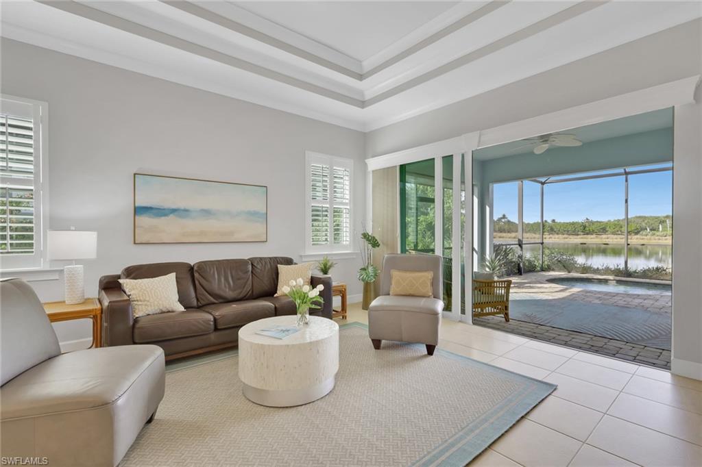 6809 Bequia Way Naples, FL 34113 - Photo 9 of 46 Living room featuring tile patterned flooring, a sunroom, a water view, a tray ceiling, and ornamental molding