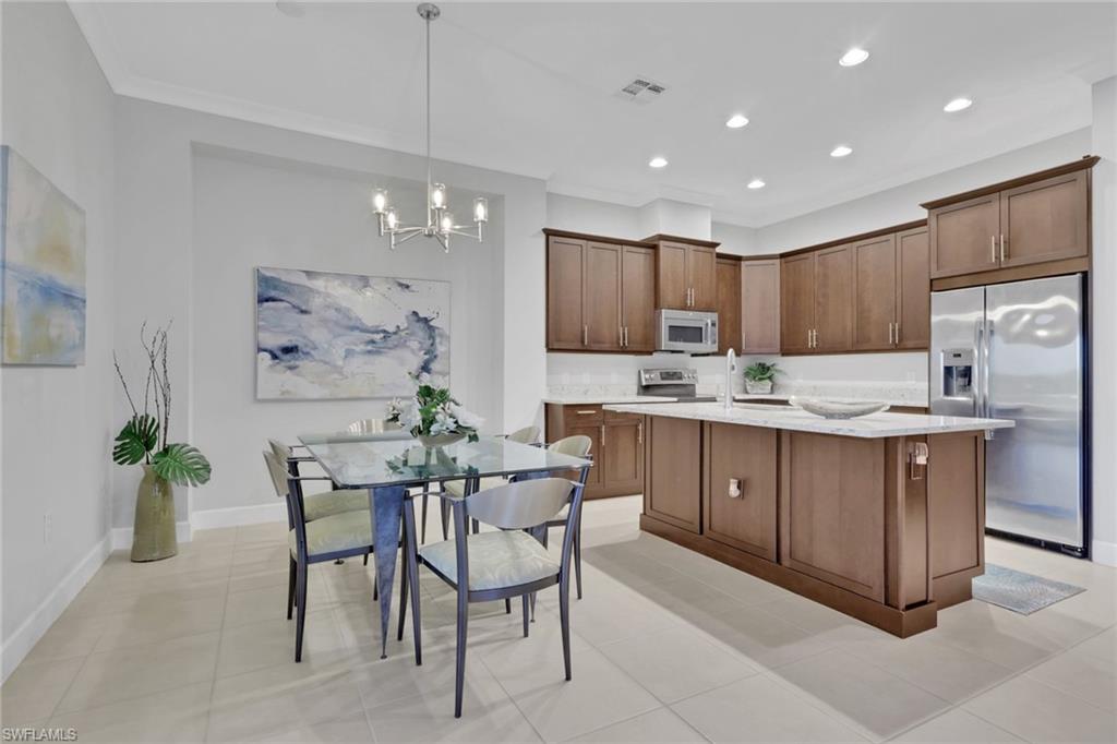 6809 Bequia Way Naples, FL 34113 - Photo 10 of 46 Kitchen featuring stainless steel appliances, decorative light fixtures, a chandelier, a center island with sink, and light stone counters