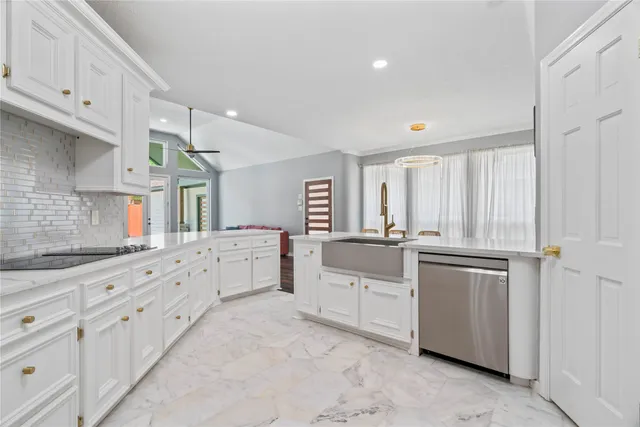 a large white kitchen with granite countertop a sink white cabinets and white appliances
