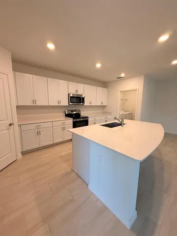 a large kitchen with kitchen island a sink a stove a oven with white cabinets