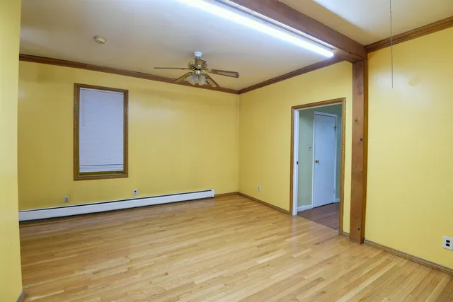 a view of an empty room with wooden floor and a ceiling fan