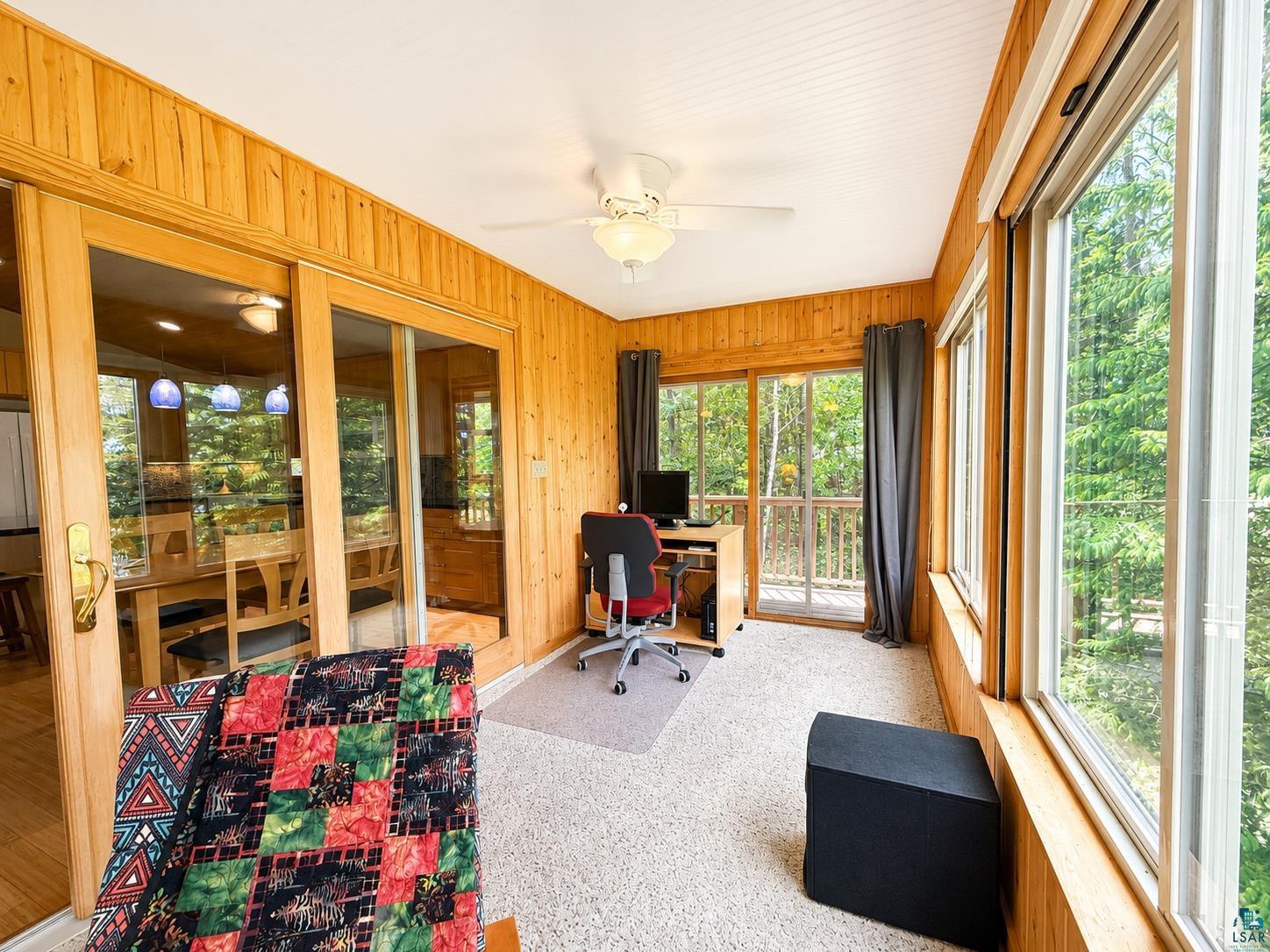 1787 North Bay Road Ely, MN 55731 - Photo 12 of 40 Sunroom featuring wood-paneled walls and ceiling, wall-to-wall carpeting, a ceiling fan with light fixture, and multiple windows overlooking exterior foliage