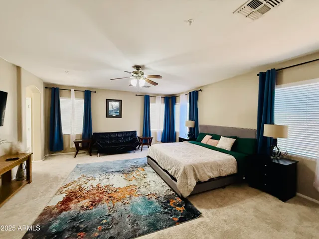 a spacious bedroom with a bed a couch and a flat tv screen on dresser