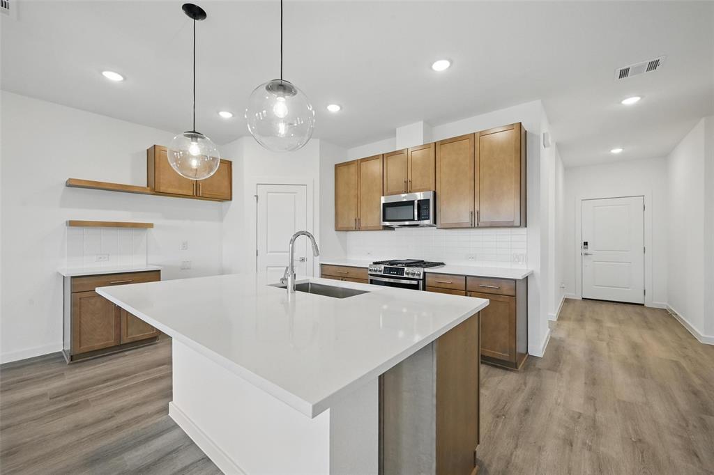 1413 Richardson Street Howe, TX 75459 - Photo 6 of 30 Modern kitchen featuring a large white island with integrated sink, stainless steel appliances, wood-finish cabinetry, white subway tile backsplash, and wood-finish flooring