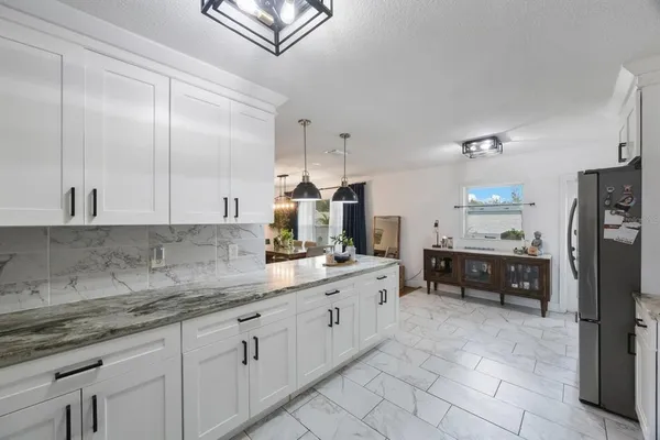 a kitchen with granite countertop a refrigerator a sink a stove and white cabinets