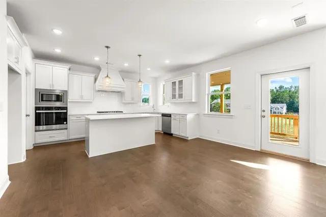 a view of kitchen with stainless steel appliances granite countertop a stove top oven a sink dishwasher a refrigerator and white cabinets with wooden floor
