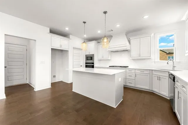 a large kitchen with stainless steel appliances kitchen island granite countertop a stove a sink a refrigerator and white cabinets with wooden floor