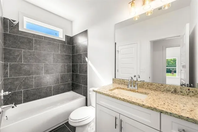 a bathroom with a granite countertop bathtub shower sink mirror vanity and toilet
