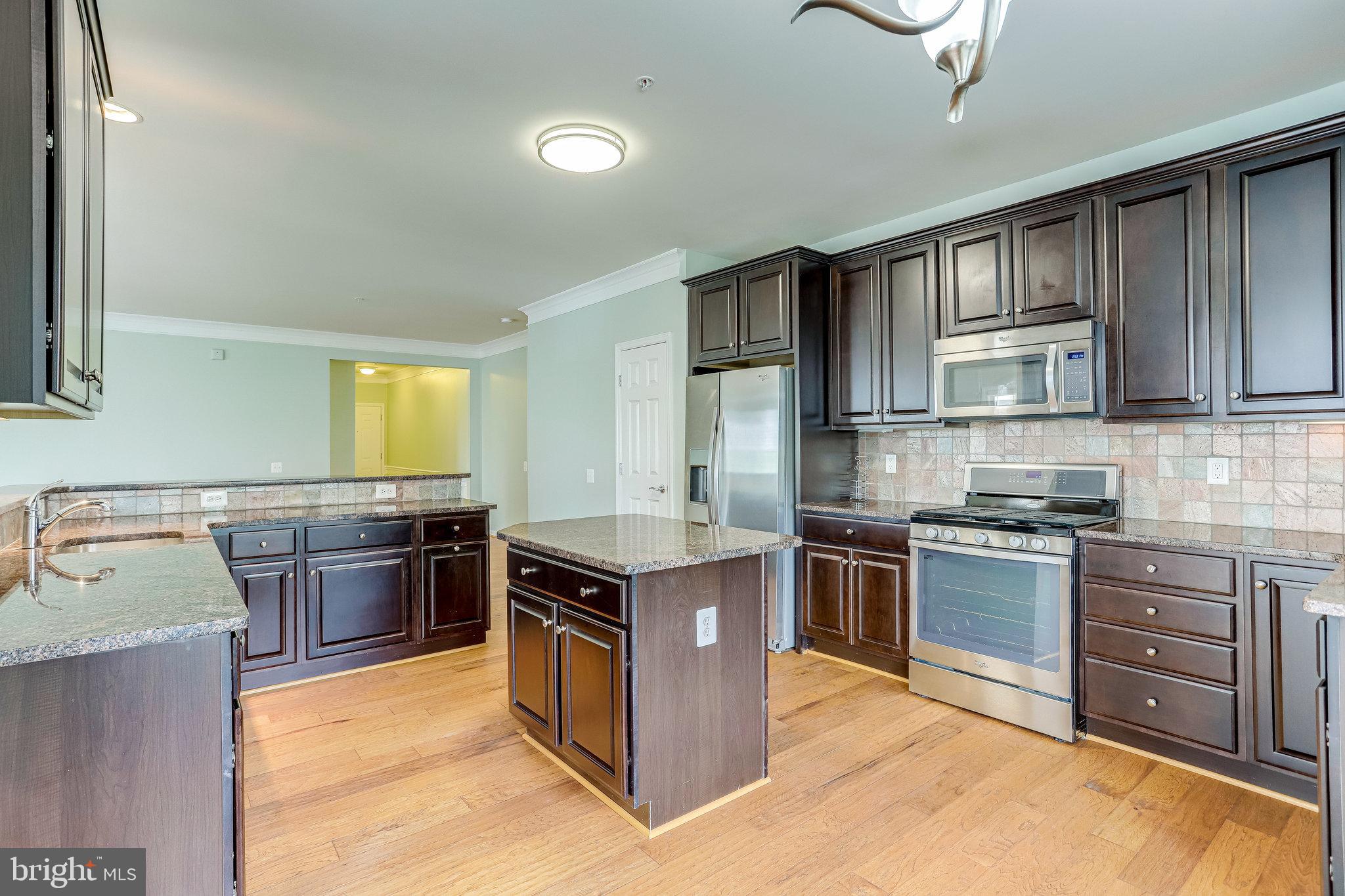 20580 Hope Spring Terrace, Unit 207 Ashburn, VA 20147 - Photo 14 of 61 a kitchen with stainless steel appliances granite countertop a stove top oven a sink dishwasher a dining table and chairs with wooden floor