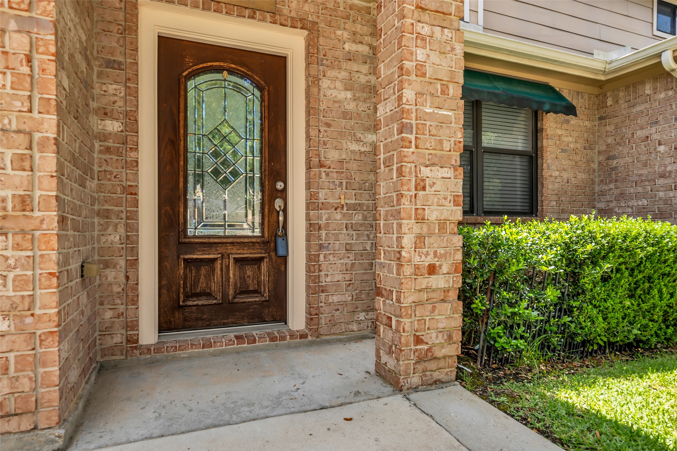 1898 Longmire Road, Unit 5 Conroe, TX 77304 - Photo 7 of 47 This photo shows a warm and inviting brick entryway with a wooden door featuring decorative glass panels. It includes a small porch area, a window with a green awning, and landscaped greenery, providing a welcoming first impression.
