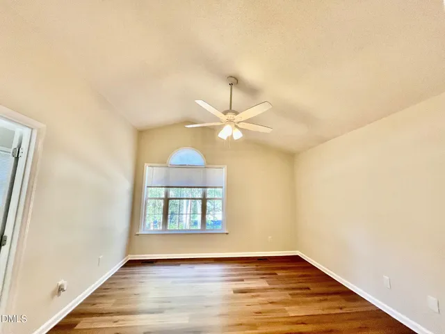 an empty room with wooden floor fan and windows