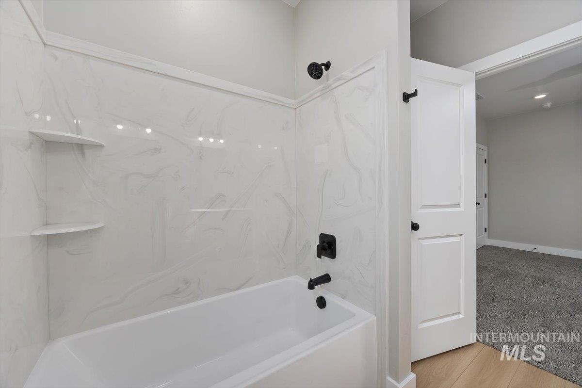 1201 Jade Drive Rupert, ID 83350 - Photo 19 of 27 Bathtub with white marble-patterned surround, integrated corner shelving, and matte black fixtures