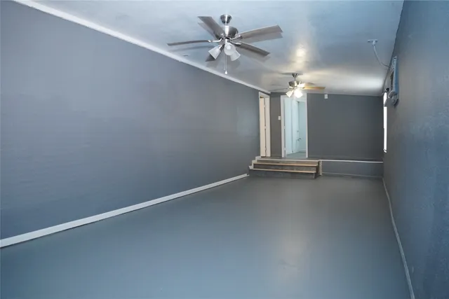 an empty room with chandelier fan and windows