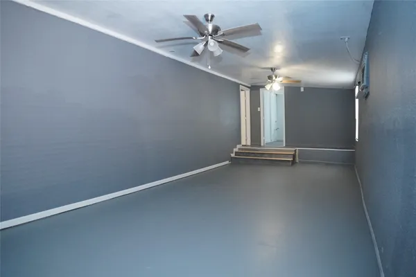 an empty room with chandelier fan and windows