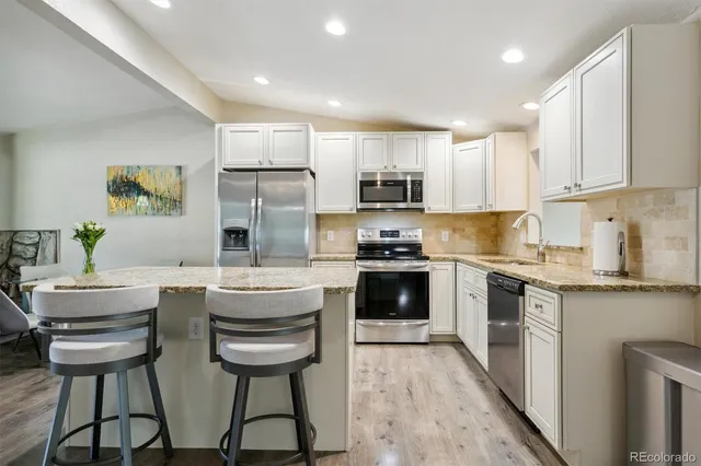 a kitchen with stainless steel appliances a stove a sink a refrigerator white cabinets and chairs