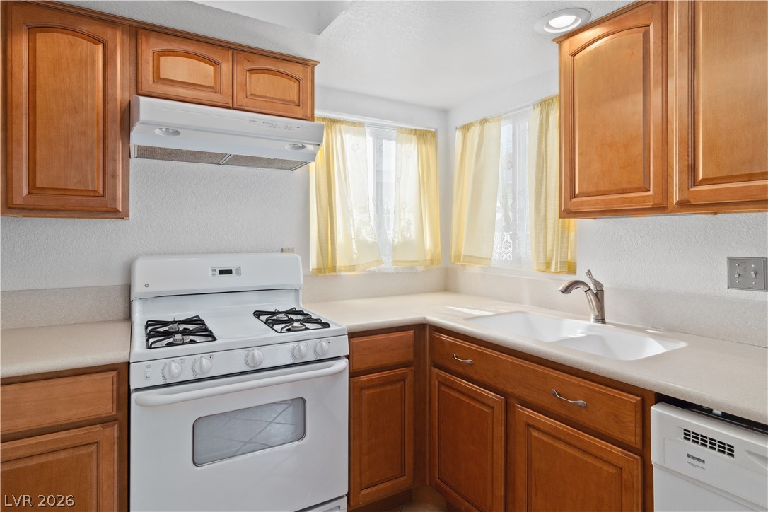 2146 High Dunes Lane Laughlin, NV 89029 - Photo 15 of 64 Kitchen with under cabinet range hood, white appliances, brown cabinets, and a sink