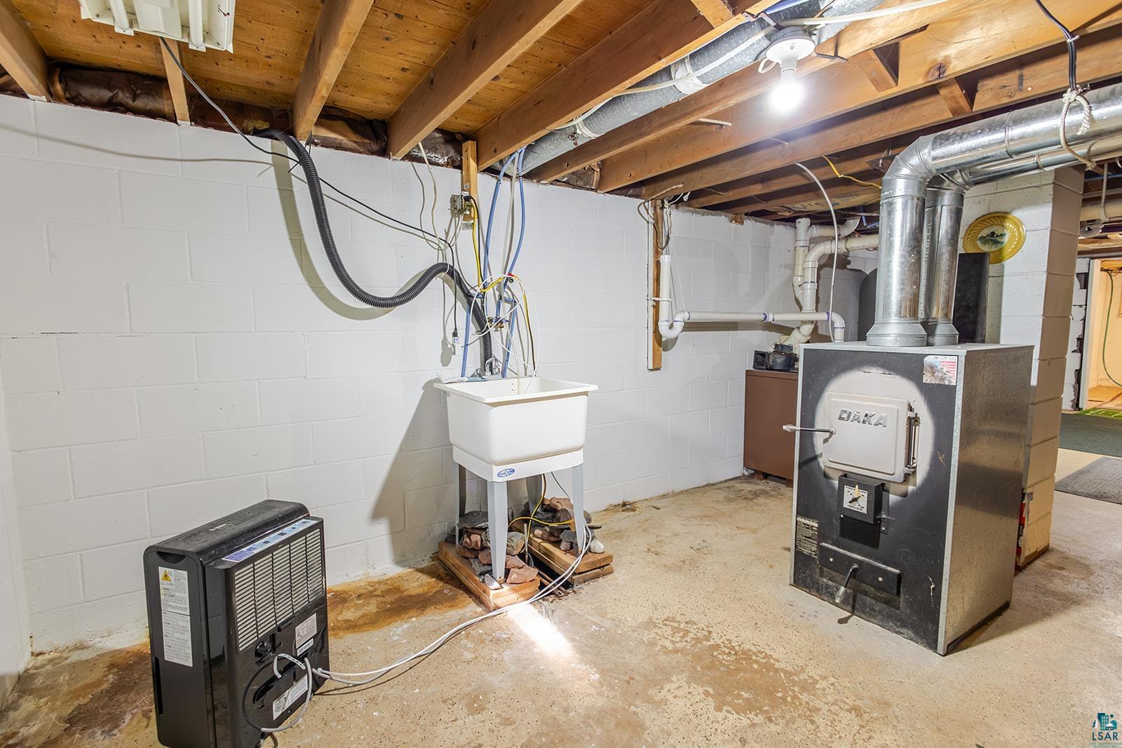 7045 Morris Thomas Road Cloquet, MN 55720 - Photo 23 of 28 Utility area featuring exposed wood ceiling joists, painted concrete block walls, a utility sink, and a wood-burning furnace with metal ductwork