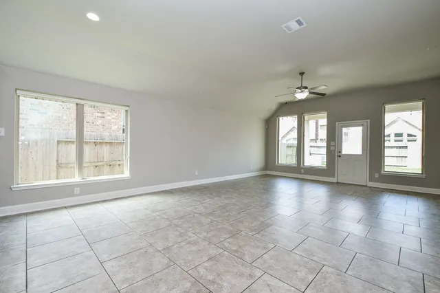 an empty room with chandelier fan and windows