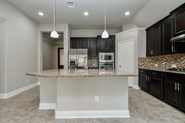 a large kitchen with a large counter top space a sink stainless steel appliances and cabinets